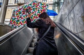 Γυναίκα ανοίγει ομπρέλα καθώς βγαίνει από τον σταθμό του ΗΣΑΠ Ομόνοια