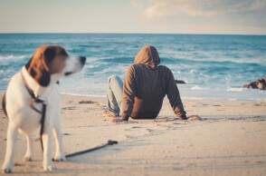 Άνδρας καθιστός στην παραλία μαζί με τον σκύλο του