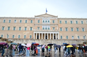 Πολίτες με ομπρέλες εν μέσω βροχής μπροστά από το μνημείο του Άγνωστου Στρατιώτη και τη Βουλή
