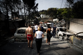 Πολίτες περπατούν ανάμεσα σε καμένα οχήματα την επομένη της τραγωδίας στο Μάτι