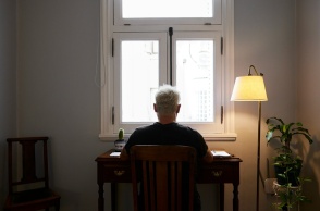 Άνδρας καθισμένος στο γραφείο του έχει την πλάτη στον φακό και βλέπει από ένα παράθυρο