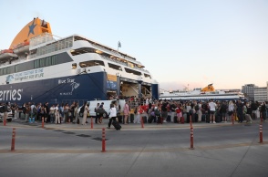 Ταξιδιώτες μπροστά από τον καταπέλτη πλοίου στο λιμάνι του Πειραιά