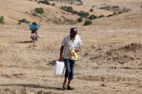 Πολίτης σε ξερό, άγονο τόπο μεταφέρει μπετόνια και μπουκάλια με νερό