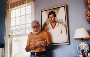 Ο Έρνεστ Χέμινγουεϊ στο σπίτι του στην Κούβα, μπροστά από το πορτρέτο του, περίπου το 1953