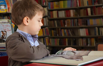 boy sitting near red table reading book