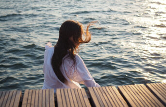 Κορίτσι καθισμένο δίπλα στη θάλασσα με γυρισμένη την πλάτη