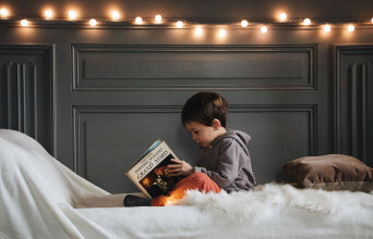 Αγοράκι καθισμένο σε κρεβάτι κρατώνας βιβλίο στα χέρια του