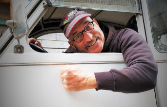 Άνδρας σε αυτοκίνητο σκυμένος στο τιμόνι κοιτάζοντας έξω από το παράθυρο το φωτογραφικό φακό