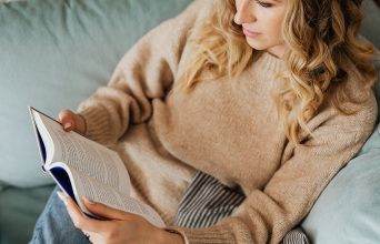 Μια γυναίκα κάθεται στον καναπέ και διαβάζει βιβλίο