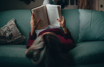 Μια κοπέλα κάθεται ανάποδα στον καναπέ και διαβάζει βιβλίο