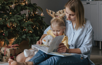 Μαμά και παιδί διαβάζουν βιβλίο δίπλα από το χριστουγεννιάτικο δέντρο