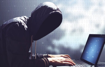 Άνθρωπος με κουκούλα και κρυμμένο πρόσωπο πληκτρολογεί σε υπολογιστή