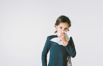 Ένα παιδί κρατάει ένα χαρτομάντηλο και κοιτάει την κάμερα. 