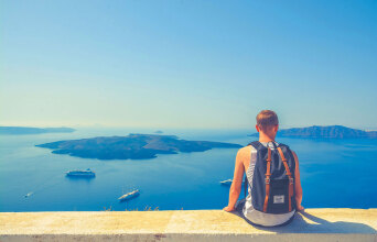 Άνδρας με σακίδιο πλάτης καθισμένος σε πεζούλι με φόντο τη θάλασσα