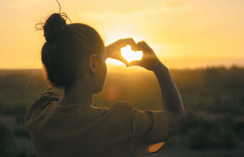 Κορίτσι σχηματίζει καρδιά με τα χέρια της με φόντο το ηλιοβασίλεμα