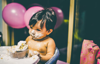 Γυμνό παιδάκι σε καρεκλάκι ταΐσματος πασαλειμμένο με τούρτα στο πρόσωπο