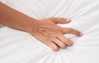 Χέρι πιάνει σεντόνι σε κρεβάτι