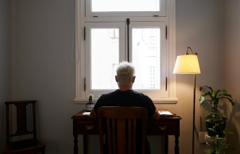 Άνδρας καθισμένος στο γραφείο του έχει την πλάτη στον φακό και βλέπει από ένα παράθυρο