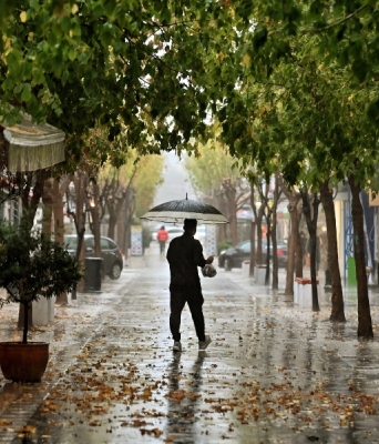 Άνδρας όρθιος με ομπρέλα στη μέση του δρόμου κατά την διάρκεια βροχής