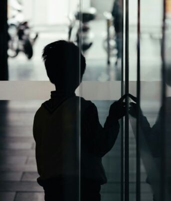 Σκιά ενός μικρού αγοριού που αγγίζει μια τζαμαρία έχοντας γυρισμένη την πλάτη στο φακό
