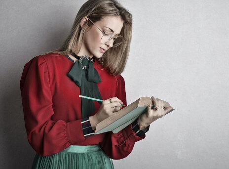 Νεαρή κοπέλα με πράσινη φούστα και κόκκινο πουκάμισο σημειώνει σε βιβλίο