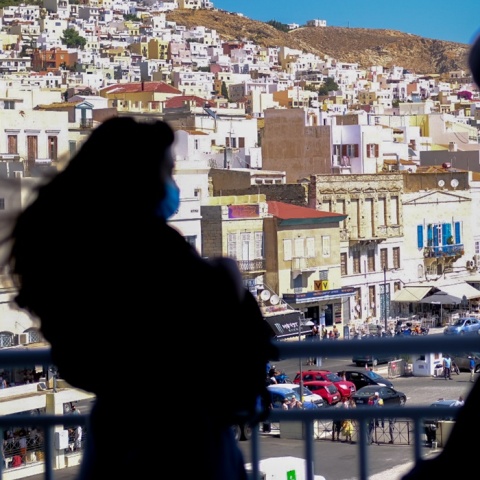 Επιβάτιδα σε κατάστρωμα πλοίο φορά τη μάσκα της - Στο φόντο σπίτια σε ελληνικό νησί