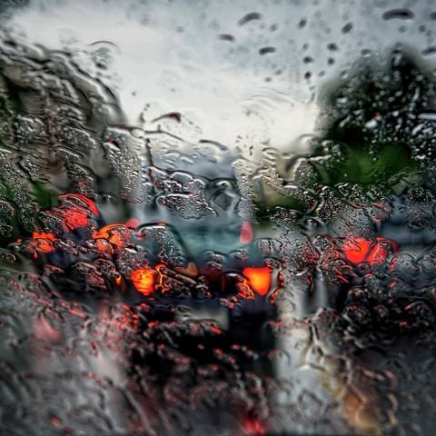 Τζάμι αυτοκινήτου γεμάτο σταγόνες βροχής και μπροστά τα φώτα από αυτοκίνητα