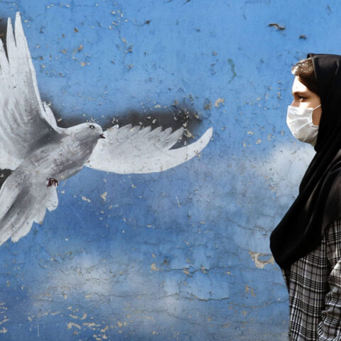 Γυναίκα με μαντίλα περνά μπροστά από mural στην Τεχεράνη