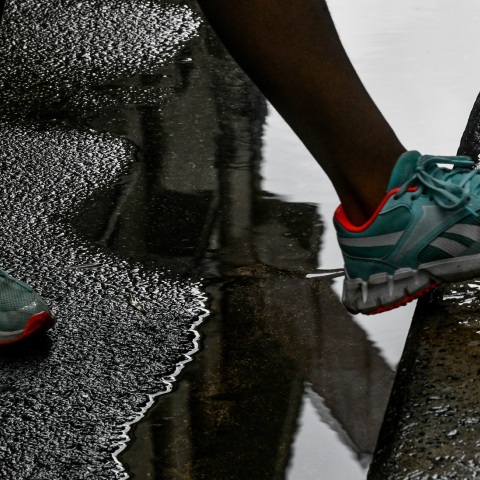 Πόδι με αθλητικό παπούτσι περνά πάω από λιμνάζοντα νερά σε δρόμο