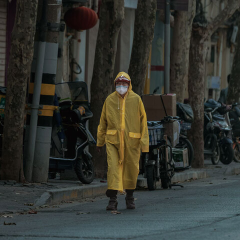 Κάτοικος στη Σανγκάη της Κίνας με αδιάβροχο και μάσκα για τον κορωνοϊό περπατά σε έρημο δρόμο της πόλης