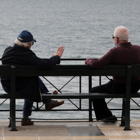 Συνταξιούχοι συνομιλούν ενώ κάθονται σε παγκάκι