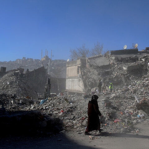 Γυναίκα ντυμένη στα μαύρα μπροστά από ισοπεδωμένα κτίρια στην πολη Καχραμανμαράς μετά τον σεισμό στην Τουρκία