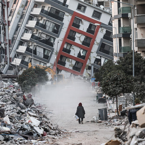 Γυναίκα στην πόλη Χατάι περπατά μπροστά από σπίτι που έχει γείρει μετά τον καταστροφικό σεισμό στην Τουρκία