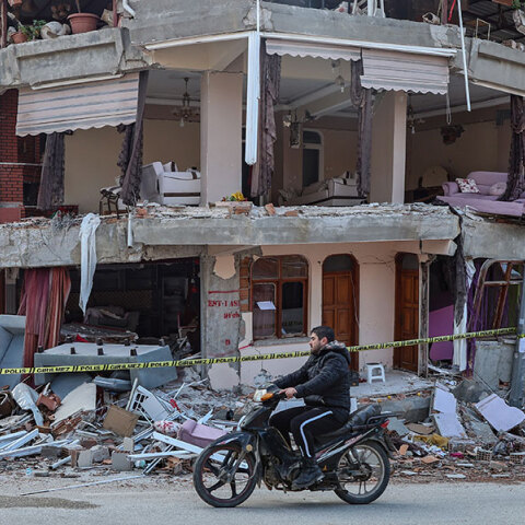 Νεαρός στην πόλη Χατάι περνά με το μηχανάκι μπροστά από κτίριο που έχει υποστεί ζημιές από τον σεισμό στην Τουρκία