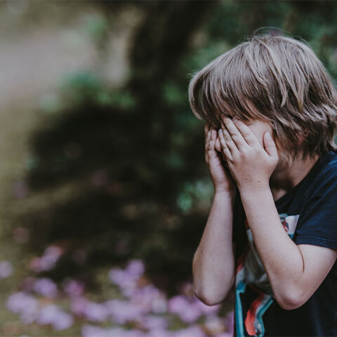 Ένα μικρό αγόρι κρύβει το πρόσωπό του με τα χέρια του