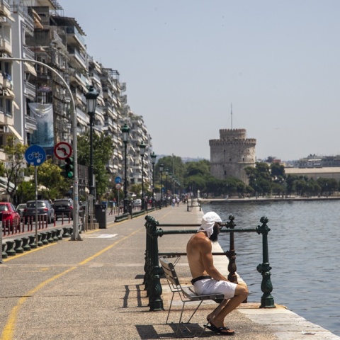 Πολίτης στη Θεσσαλονίκη καθισμένος σε παγκάκι εν μέσω καύσωνα φορά την μπλούζα του στο κεφάλι - Φόντο ο Λευκός Πύργος