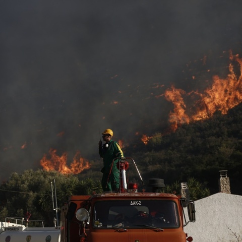 Πυροσβέστης πάνω στο όχημα δίνει οδηγίες μέσω ασυρμάτου - Από πίσω του οι φωτιές στον Κουβαρά
