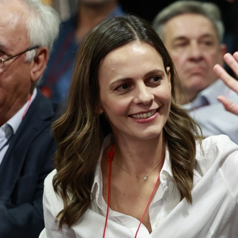 Η Έφη Αχτσιόγλου με σηκωμένο το χέρι χαιρετά και χαμογελά