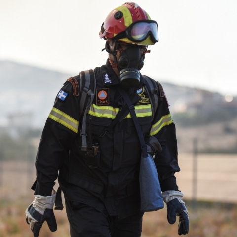 Πυροσβέστης με μπλε στολή, κράνος, μάσκα και γυαλιά προστασίας σε πυρκαγιά στην Λαμία