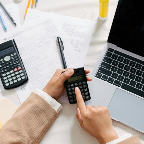 Δύο χέρια χειρίζονται calculator πάνω από ένα laptop μαζί με λογιστικά έγγραφα