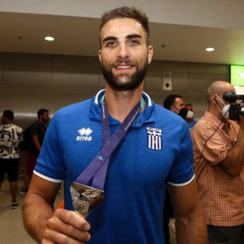 Ο Στέφανος Ντούσκος κρατώντας ένα μεταλλείο φορώντας μπλε αθλητική μπλούζα