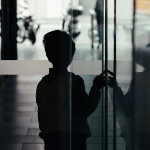 Σκιά ενός μικρού αγοριού που αγγίζει μια τζαμαρία έχοντας γυρισμένη την πλάτη στο φακό