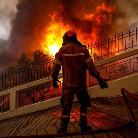 πυροσβέστης με καφέ στολή και μάσκα μπροστά από φωτιά