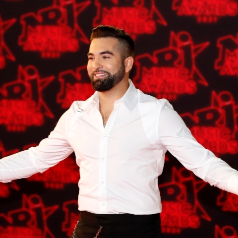 Ο Γάλλος τραγουδιστής Kendji Girac με ανοιχτά τα χέρια με άσπρο πουκάμισο και μαύρο παντελόνι