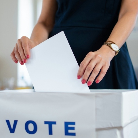 Γυναικεία χέρια ρίχνουν ψηφοδέλτιο σε κάλπη που γράφει vote