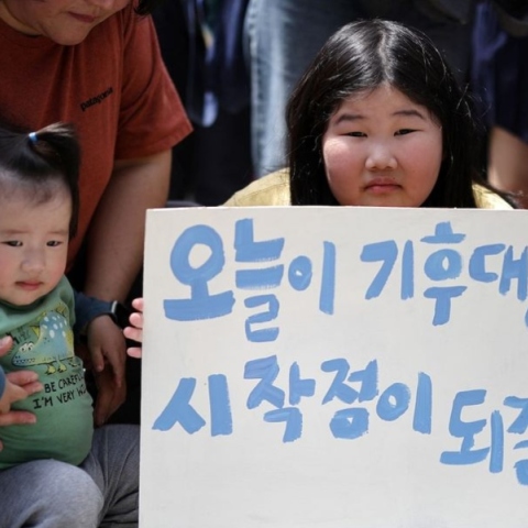 Νεαρή Κορεατισσα κρατάει πινακίδα δίπλα σε γονέα με ένα μωρό