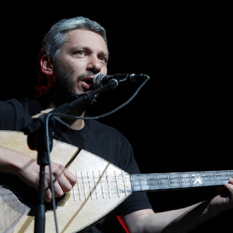 Ο Αλκίνοος Ιωαννίδης καθιστός μπροστά σε μικρόφωνο τραγουδάει κρατώντας λάουτο