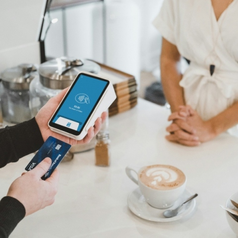 Δύο χέρια σκανάρουν κάρτα σε pos μπροστά από γυναίκα με άσπρο φόρεμα