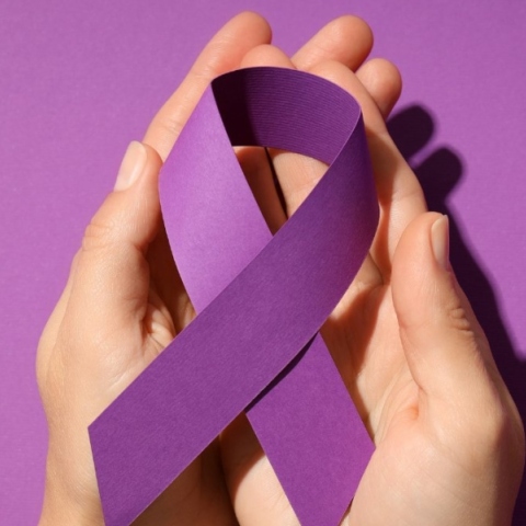 Δύο χέρια κρατάν μωβ κορδέλα