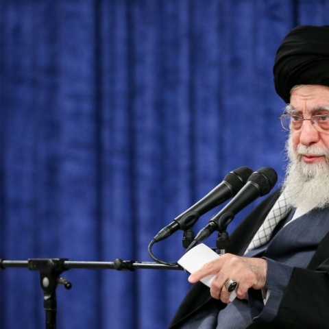 άνδρας με γενειάδα καθιστός, μικρόφωνο, σημαία